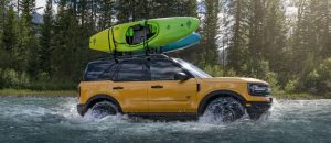 A yellow 2021 Ford Bronco Sport with kayaks on the roof rack driving through a creek near Waco, TX